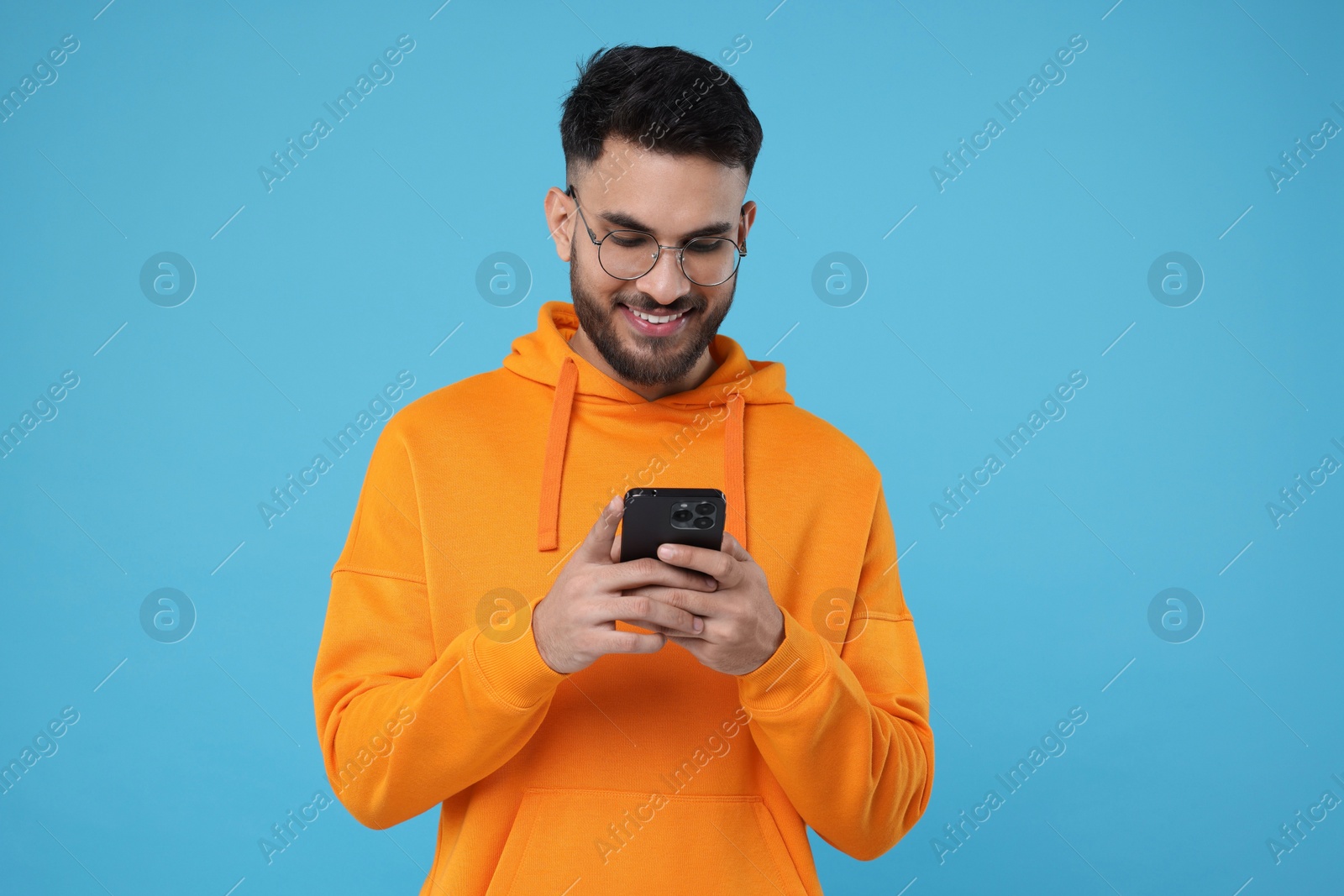 Photo of Happy young man using smartphone on light blue background