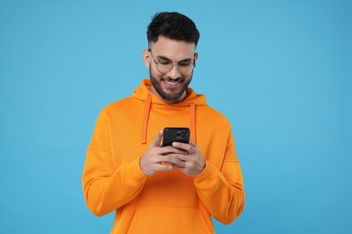 Happy young man using smartphone on light blue background