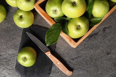 Ripe green apples with water drops, cutting board and knife on grey table, flat lay