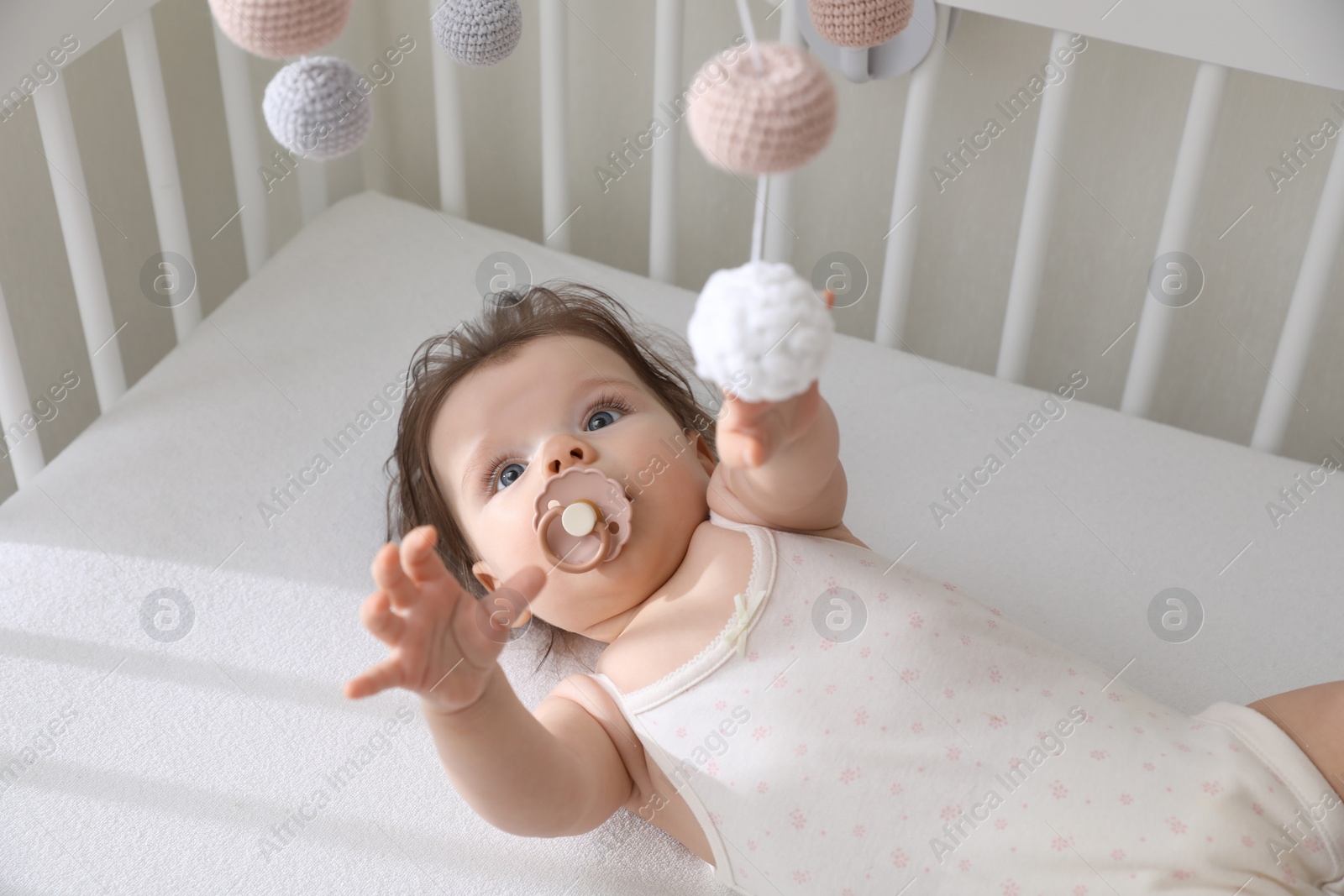 Photo of Cute little baby looking at hanging mobile in crib