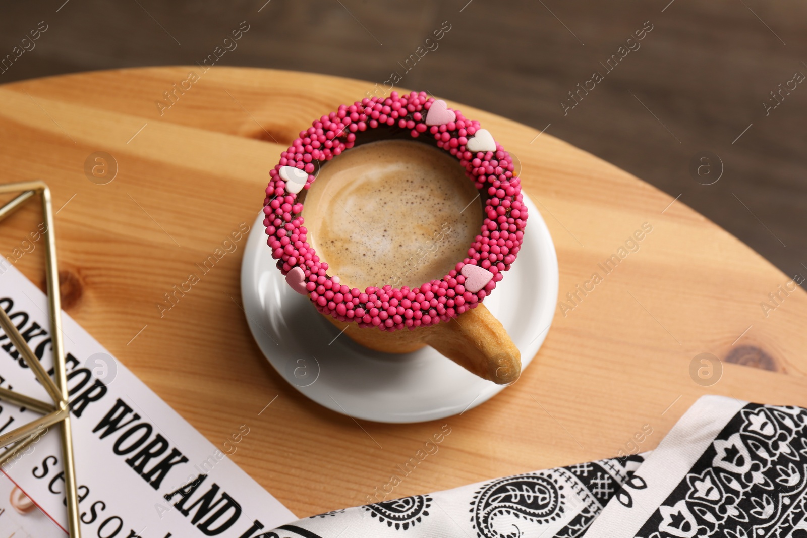 Photo of Delicious edible biscuit cup of coffee decorated with sprinkles on wooden table, above view