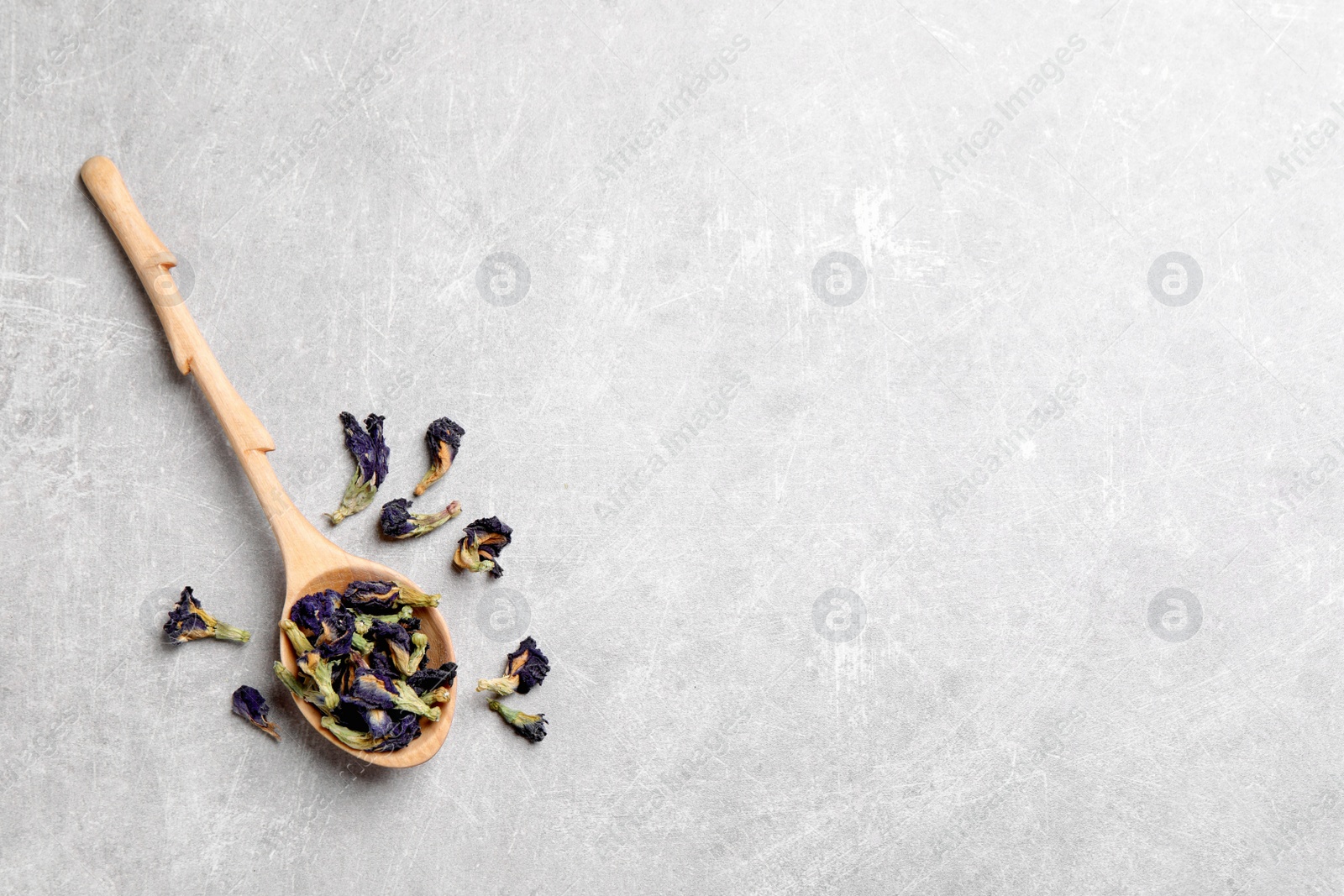 Photo of Spoon and dry organic blue Anchan on light grey table, flat lay with space for text. Herbal tea