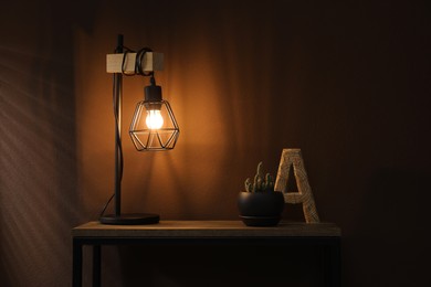 Stylish lamp, decor and green plant on wooden table near brown wall indoors. Interior design