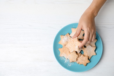 Woman taking tasty homemade Christmas cookie from plate on table, top view
