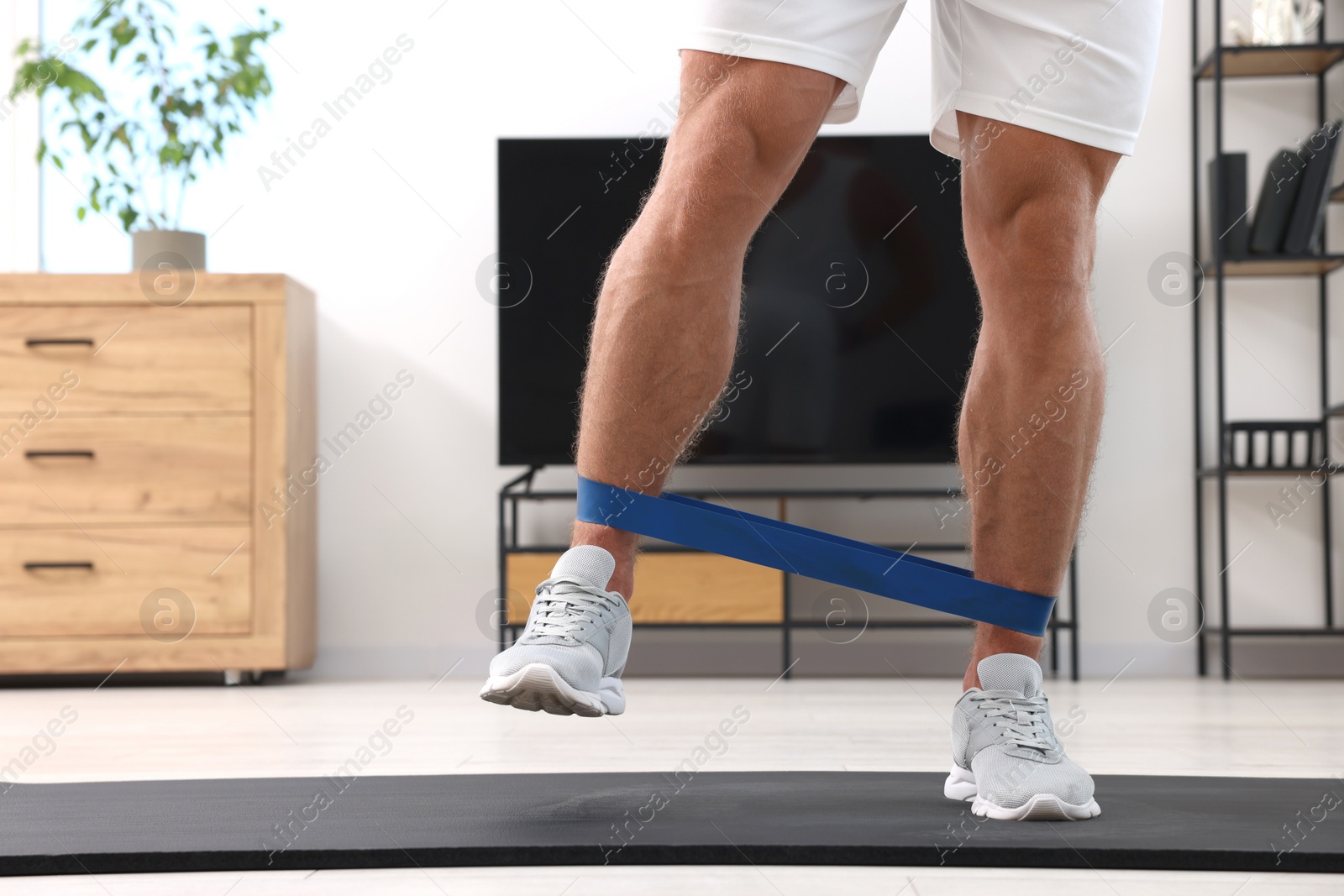 Photo of Athletic man doing exercise with elastic resistance band on mat at home, closeup