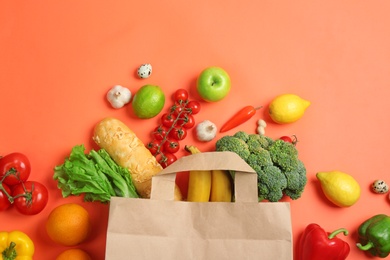 Photo of Paper bag with different groceries on coral background, flat lay