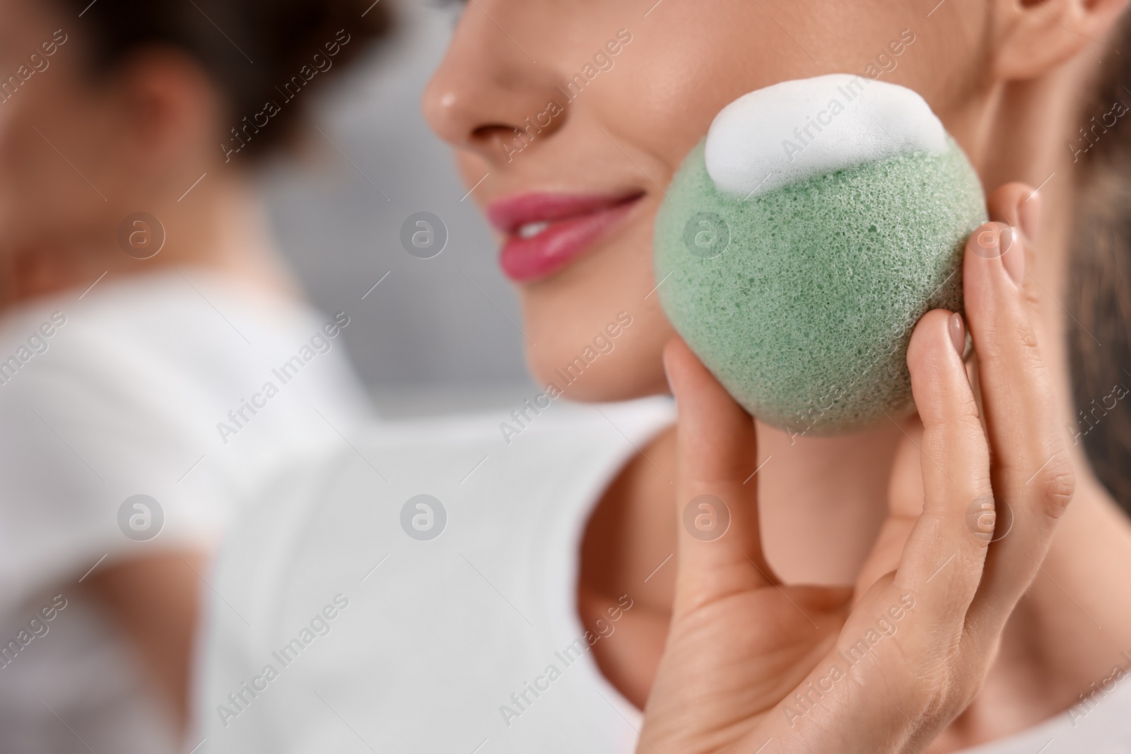 Photo of Happy young woman washing her face with sponge in bathroom, closeup