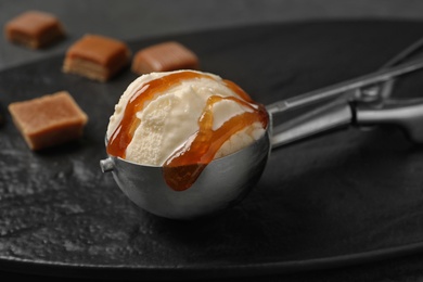 Photo of Scoop of ice cream with caramel sauce on slate plate, closeup