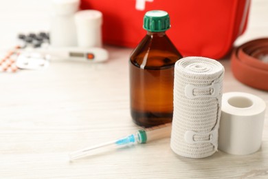 Photo of Bandage, sticking plaster roll, syringe and medicament on white wooden table, space for text. First aid kit