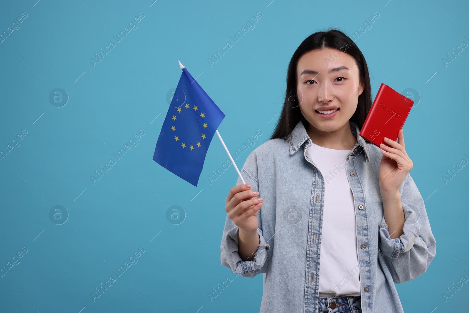 Photo of Immigration to European Union. Happy woman with passport and flag on light blue background, space for text