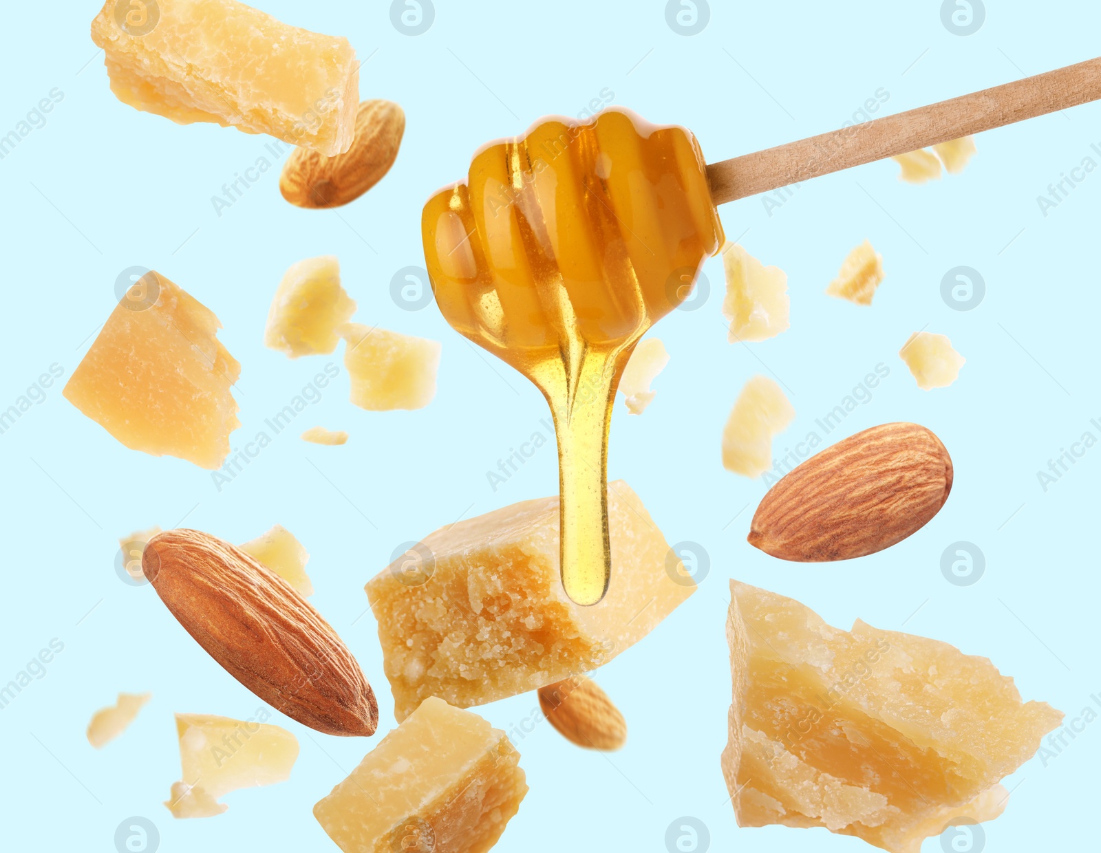 Image of Pieces of delicious parmesan, almonds and honey falling on light blue background