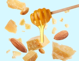 Image of Pieces of delicious parmesan, almonds and honey falling on light blue background