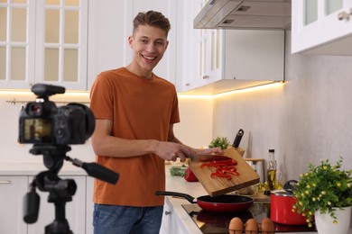 Photo of Smiling food blogger cooking while recording video in kitchen