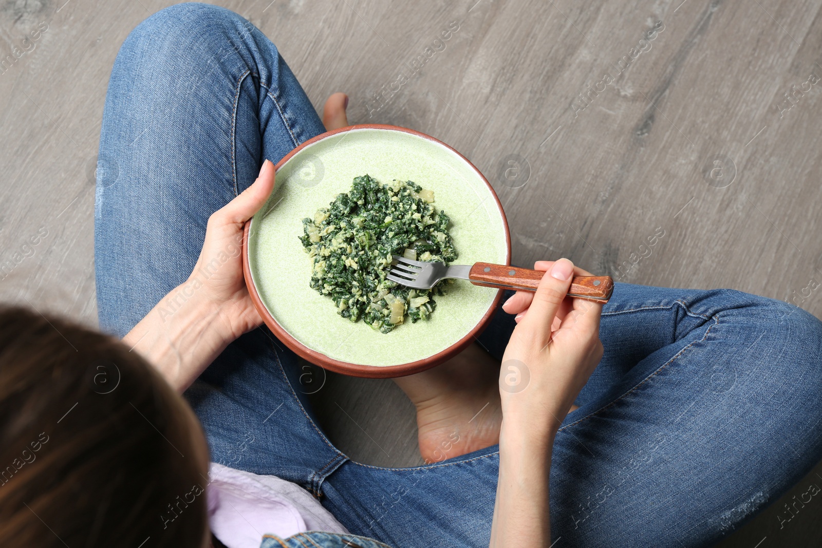 Photo of Young woman with plate of tasty spinach on wooden floor, closeup. Healthy food