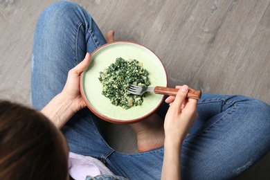 Photo of Young woman with plate of tasty spinach on wooden floor, closeup. Healthy food