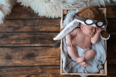 Photo of Cute newborn baby in aviator hat sleeping on wooden background, top view. Space for text