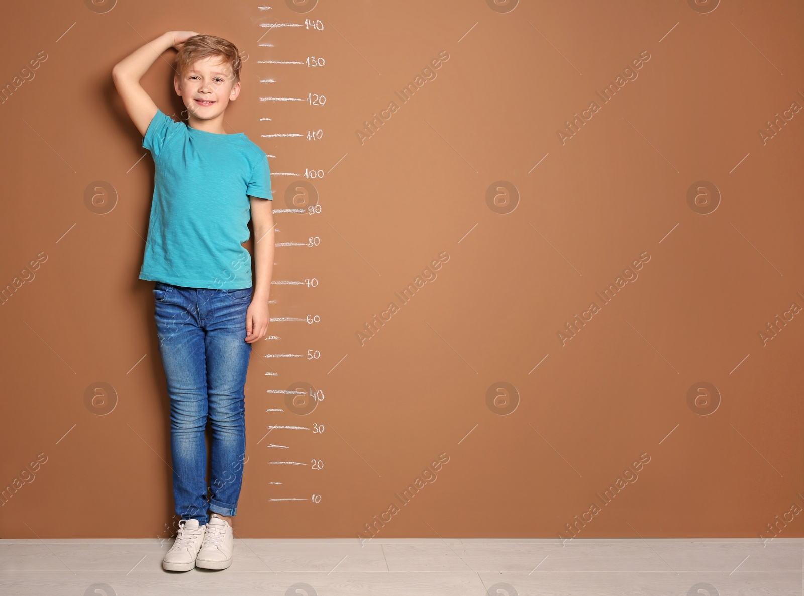 Photo of Little boy measuring his height near color wall