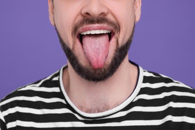 Photo of Happy man showing his tongue on purple background, closeup