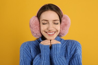 Photo of Happy woman wearing warm earmuffs on yellow background