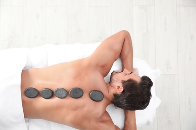 Photo of Young man receiving hot stone massage in spa salon, top view. Space for text