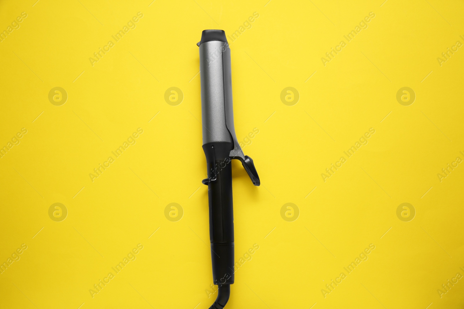 Photo of Hair curling iron on yellow background, top view