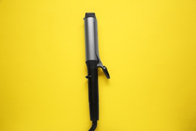 Photo of Hair curling iron on yellow background, top view