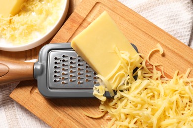 Photo of Grated, whole piece of cheese and grater on table, top view