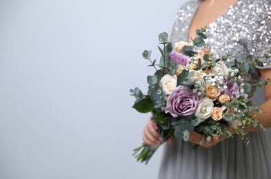 Bride holding beautiful wedding bouquet on light grey background, closeup. Space for text