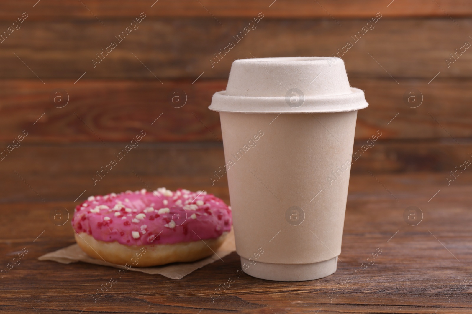 Photo of Tasty frosted donut with sprinkles and hot drink on wooden table