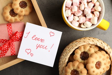 Photo of Note with phrase I love You near gift box, cookies and cup of hot drink on dark table, flat lay