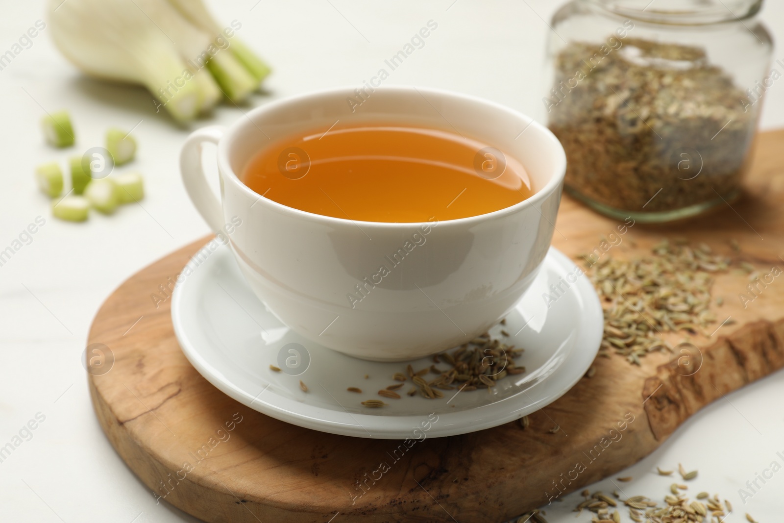 Photo of Fennel tea in cup, seeds and fresh vegetable on white table, closeup