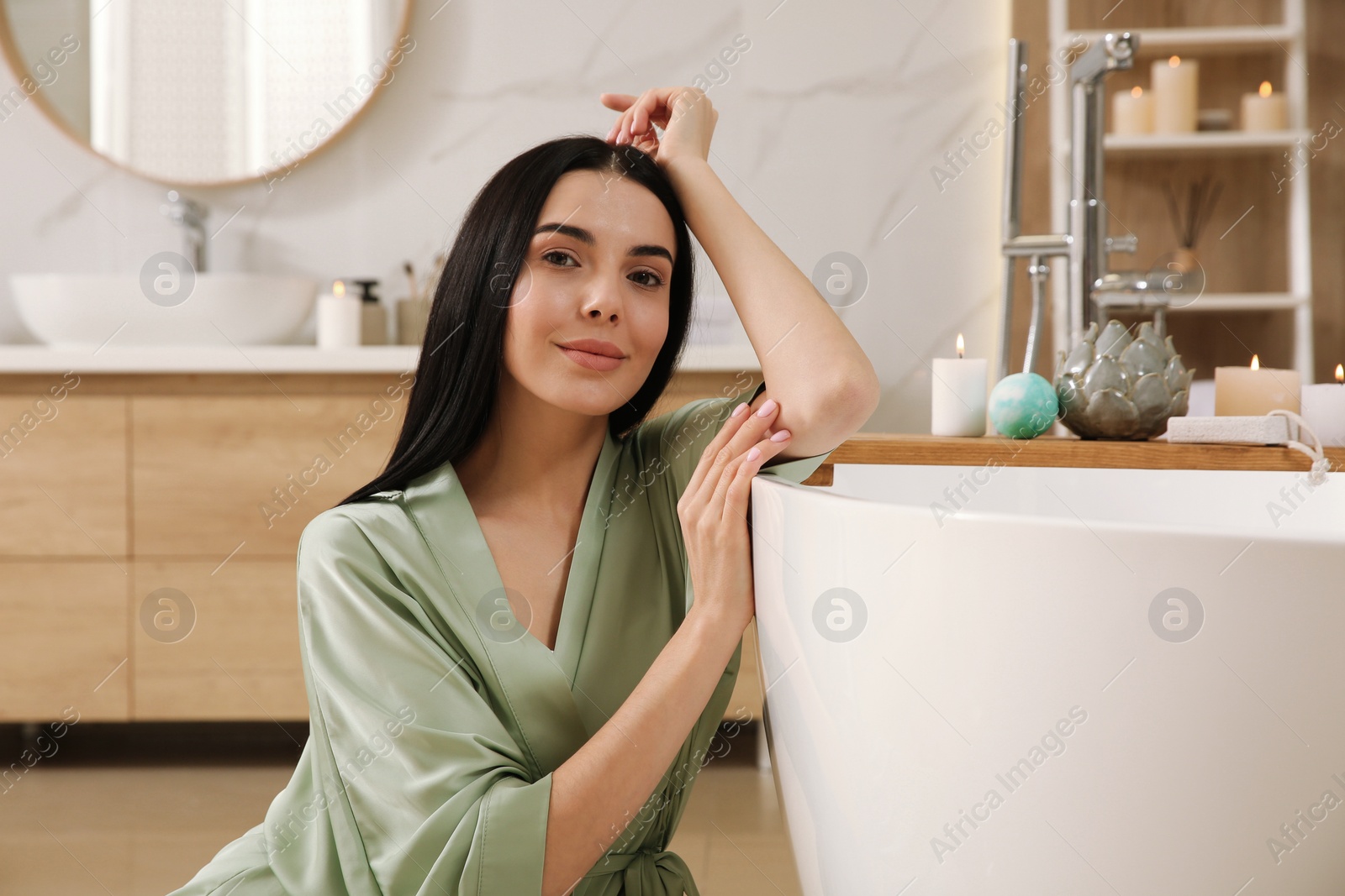 Photo of Beautiful young woman sitting near tub in bathroom