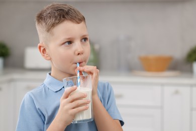 Cute boy drinking fresh milk from glass indoors, space for text