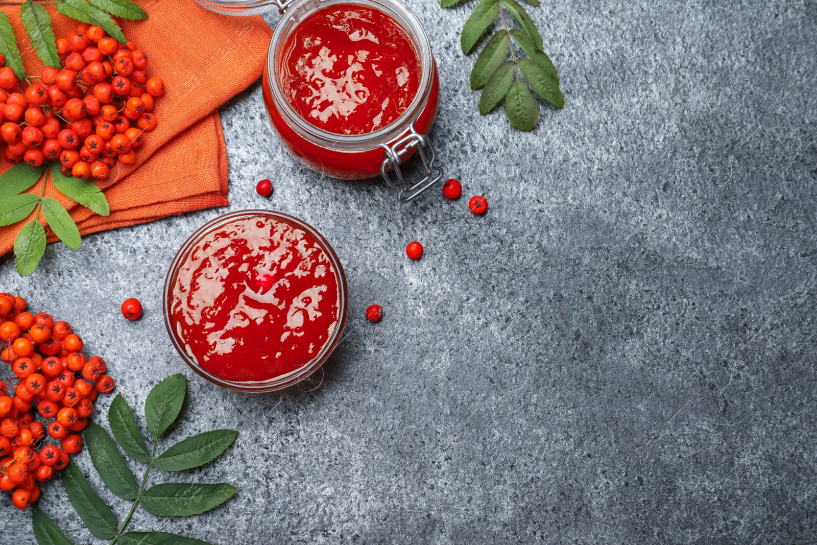 Photo of Flat lay composition with delicious rowan jam and berries on grey table. Space for text