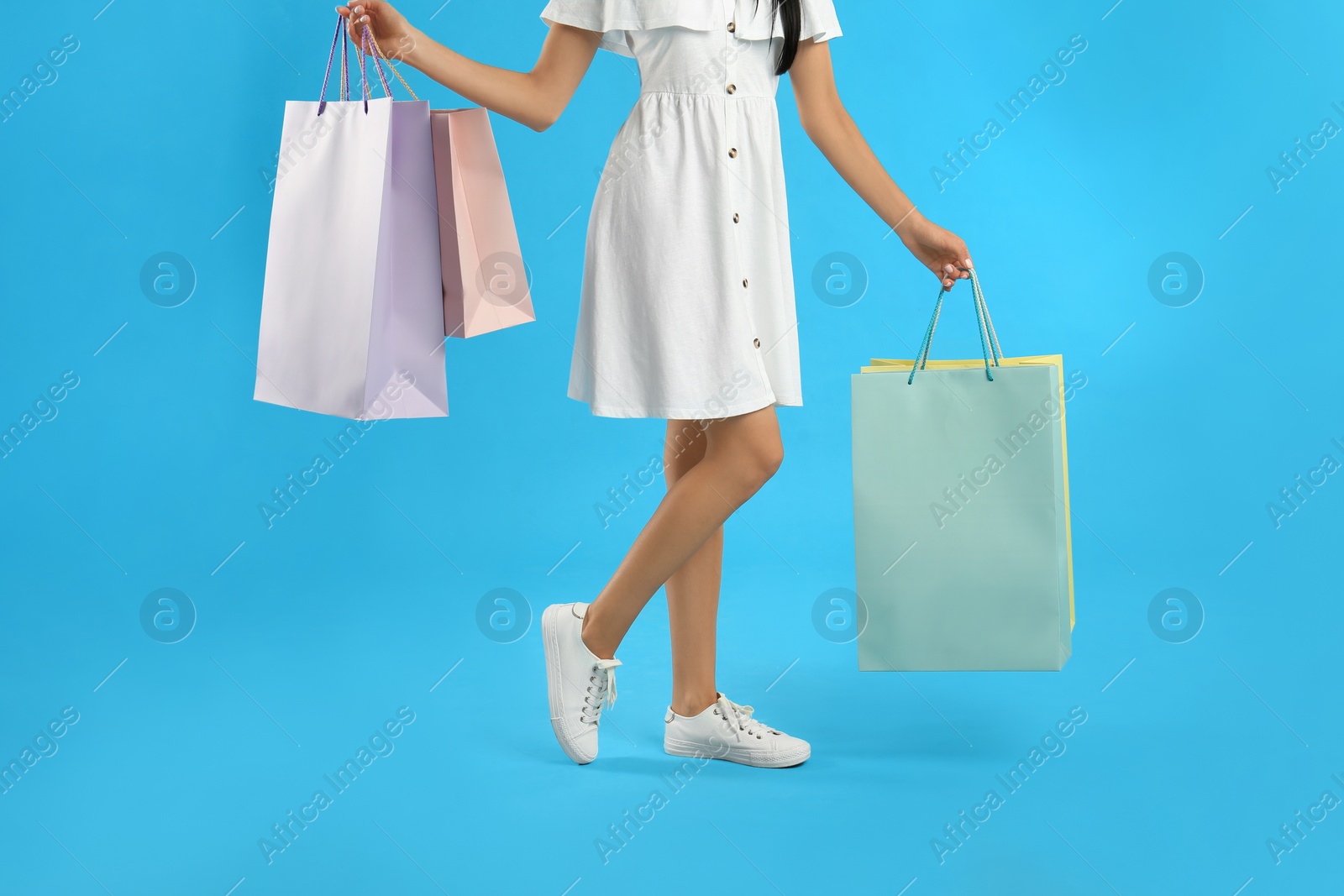 Photo of Young woman with paper shopping bags on light blue background, closeup