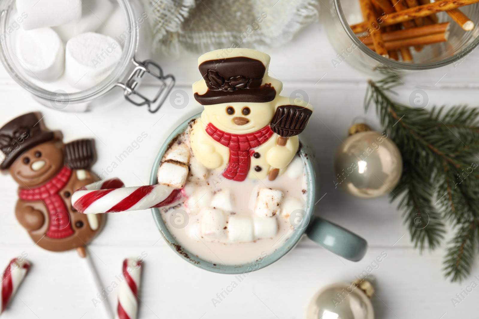 Photo of Flat lay composition with chocolate snowman candy in cup of drink on white wooden table