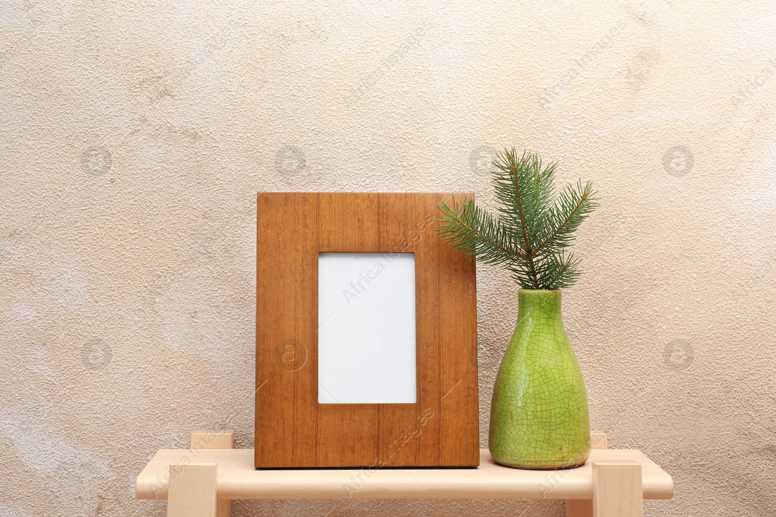 Photo of Blank frame and vase with fir branch on table near color wall. Mock up for design