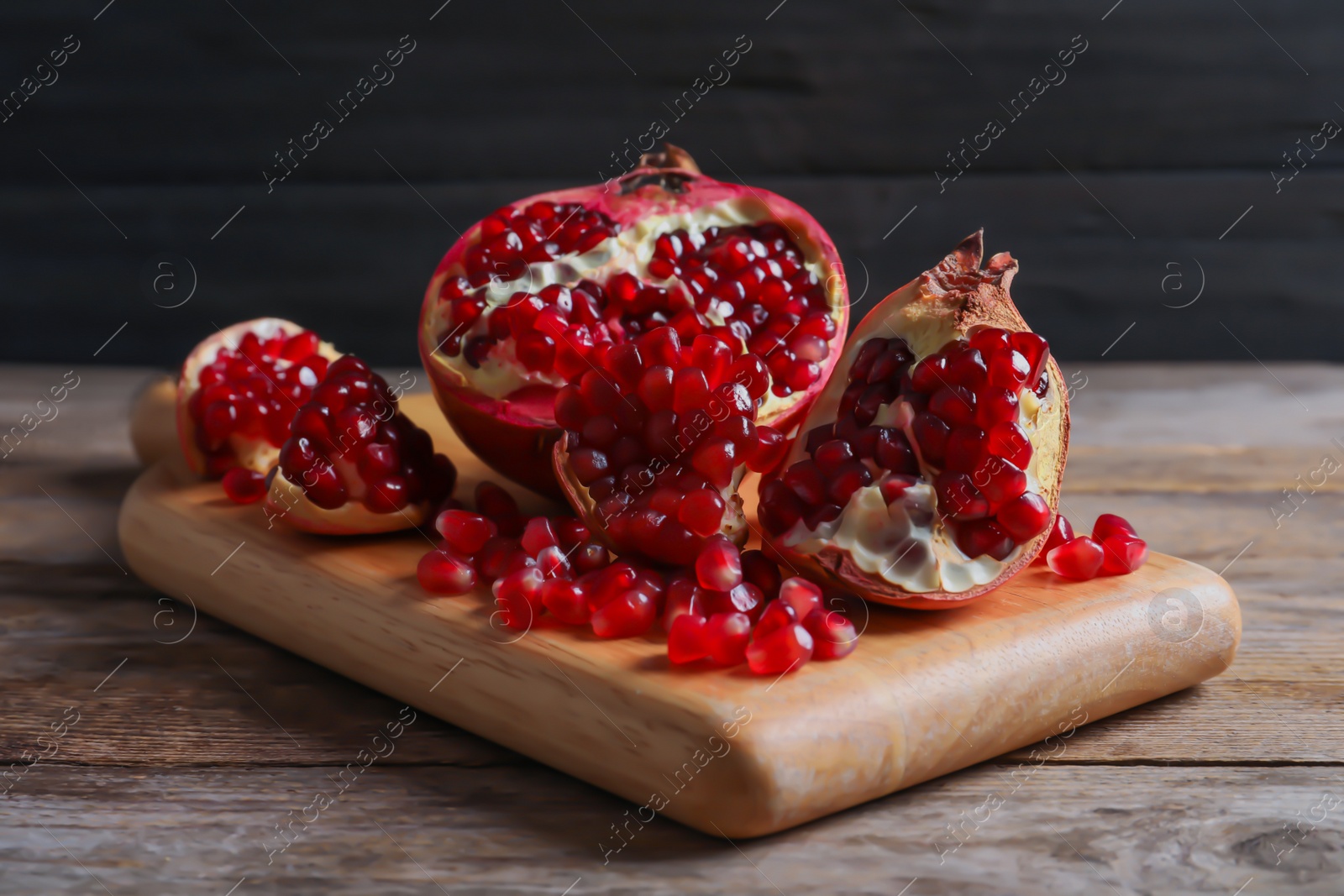 Photo of Board with ripe pomegranates and seeds on wooden table