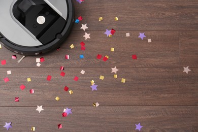 Modern robotic vacuum cleaner removing confetti from wooden floor, top view. Space for text