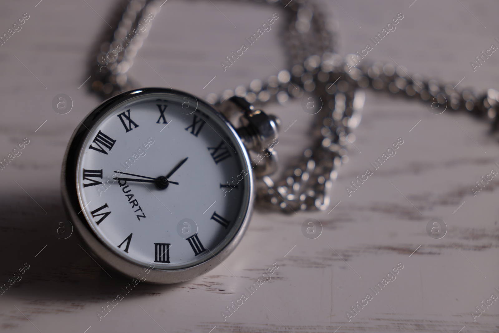 Photo of Silver pocket clock with chain on grey wooden table, closeup