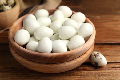 Photo of Many peeled boiled quail eggs and another one in shell on wooden table, closeup