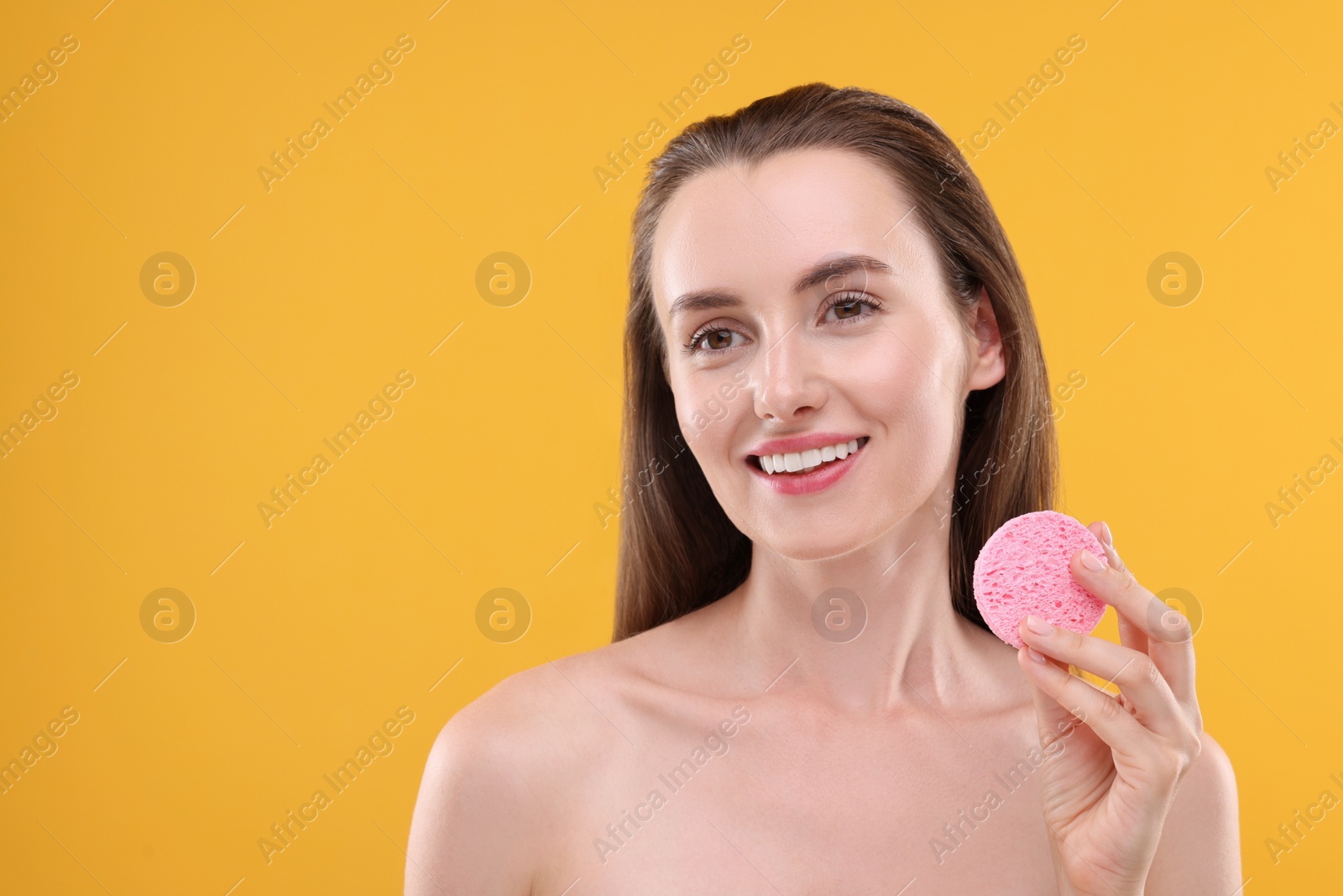 Photo of Happy young woman holding face sponge on orange background. Space for text