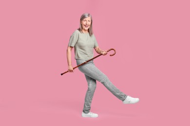 Photo of Cheerful senior woman with walking cane posing on pink background
