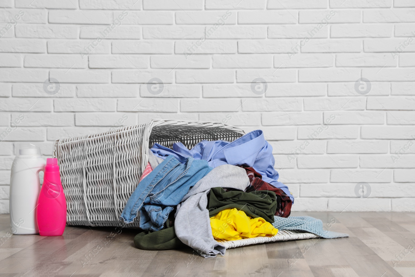 Photo of Laundry basket, dirty clothes and detergents on floor near brick wall. Space for text