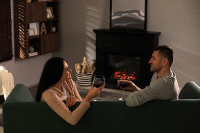 Photo of Lovely couple with glasses of wine spending time together on sofa near fireplace at home