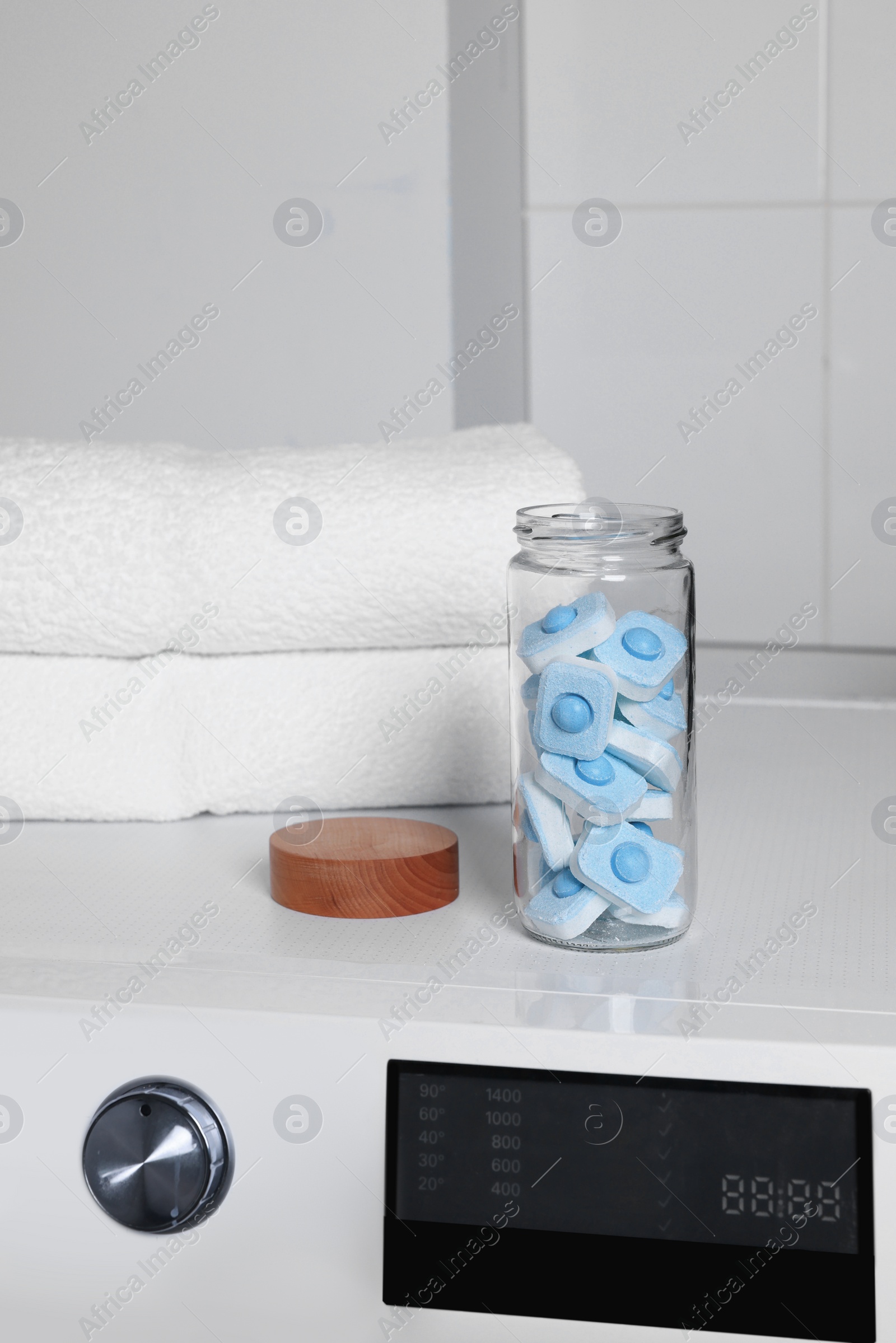 Photo of Glass jar with water softener tablets on washing machine in bathroom