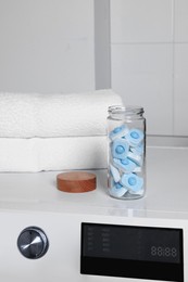 Photo of Glass jar with water softener tablets on washing machine in bathroom