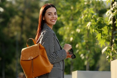 Beautiful young woman with stylish backpack in park