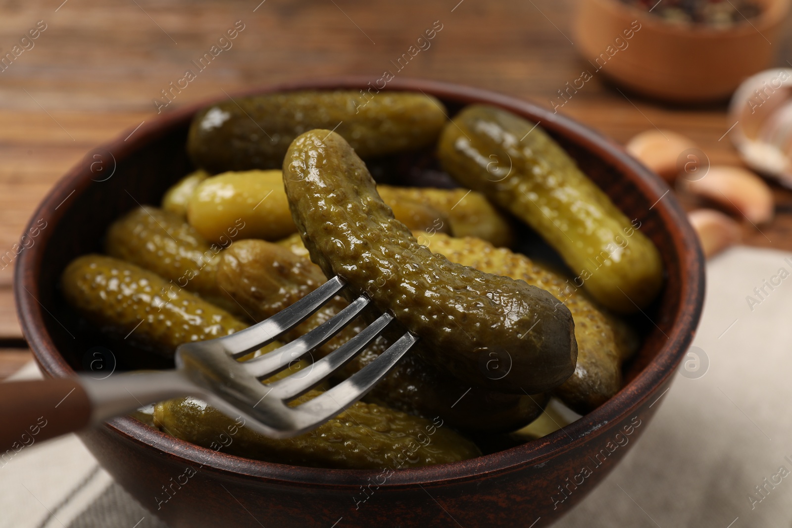 Photo of Fork with pickled cucumber over bowl on table, closeup
