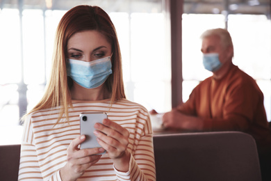 Photo of Woman with medical mask and mobile phone in cafe. Virus protection
